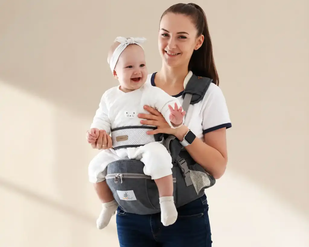 Mother carrying cheerful baby in a grey hip seat baby carrier